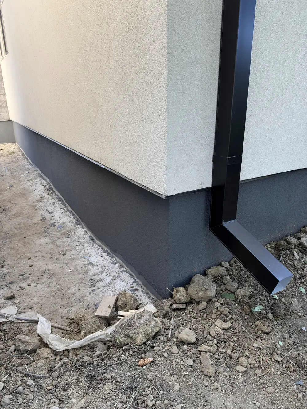 Finished grey acrylic foundation corner beside a black downspout