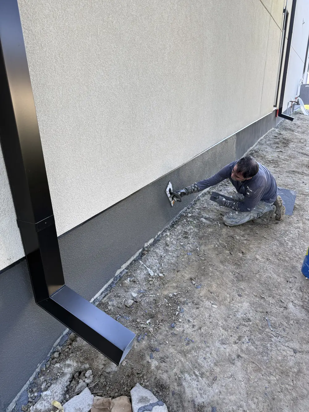 Crew member working on the foundation coating beside the house